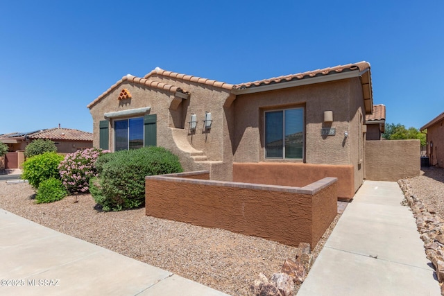 view of front facade with stucco siding, a tile roof, and fence