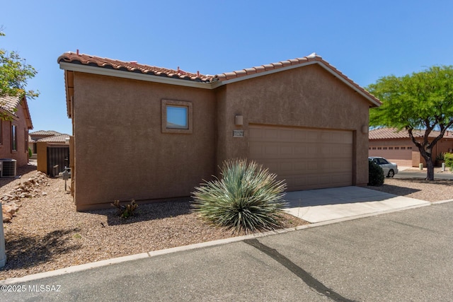 view of front of home with an attached garage, central AC, stucco siding, a tiled roof, and driveway