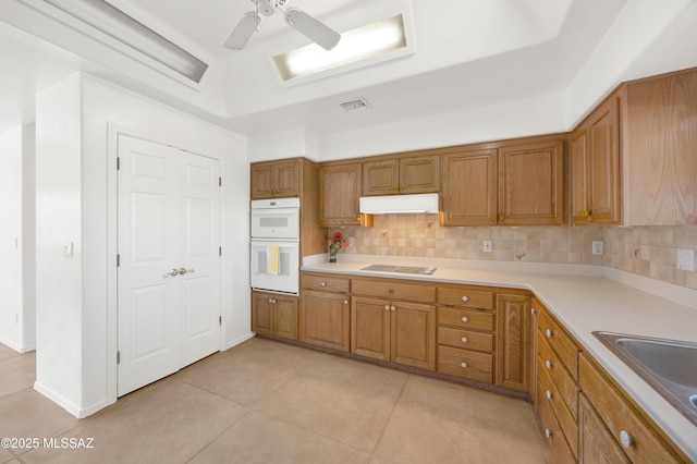 12471 E Speedway Blvd, Tucson, AZ 85748 - kitchen with under cabinet range hood, brown cabinetry, double oven, backsplash, and light tile patterned flooring