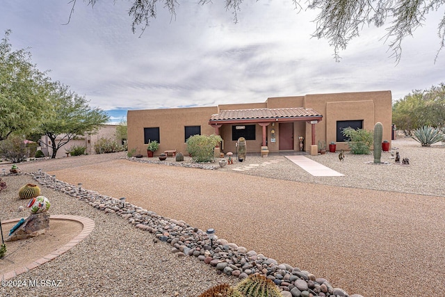 pueblo-style home featuring a garage, stucco siding, gravel driveway, and a tiled roof