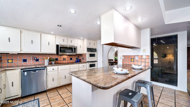900 N Camino Del Codorniz, Tucson, AZ 85749 - kitchen with stainless steel appliances, light tile patterned floors, decorative backsplash, white cabinetry, and a peninsula