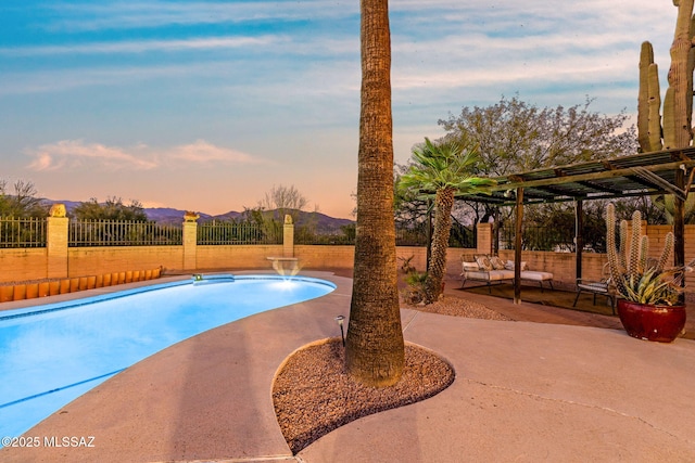 900 N Camino Del Codorniz, Tucson, AZ 85749 - pool at dusk featuring a patio, a mountain view, and an outdoor hangout area