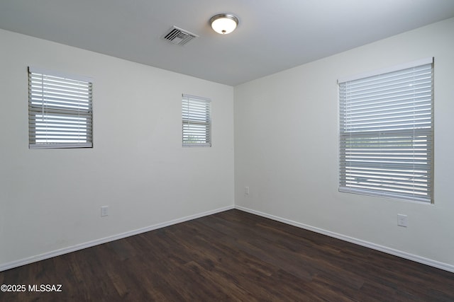 unfurnished room featuring baseboards, visible vents, and dark wood-type flooring