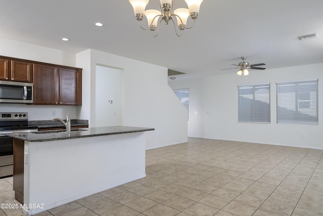 kitchen featuring dark brown cabinetry, visible vents, appliances with stainless steel finishes, a sink, and dark stone counters
