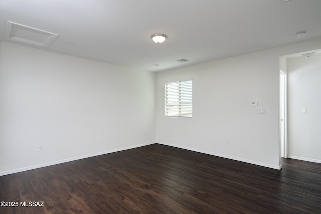 spare room featuring baseboards, attic access, dark wood-style floors, and visible vents