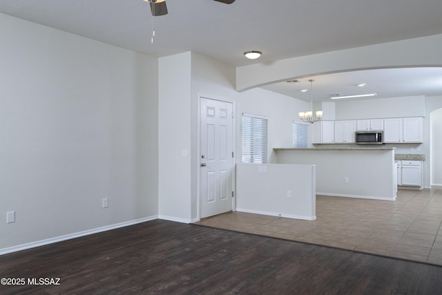 493 E Placita Nodo, Sahuarita, AZ 85629 - unfurnished living room featuring baseboards, arched walkways, ceiling fan with notable chandelier, and wood finished floors