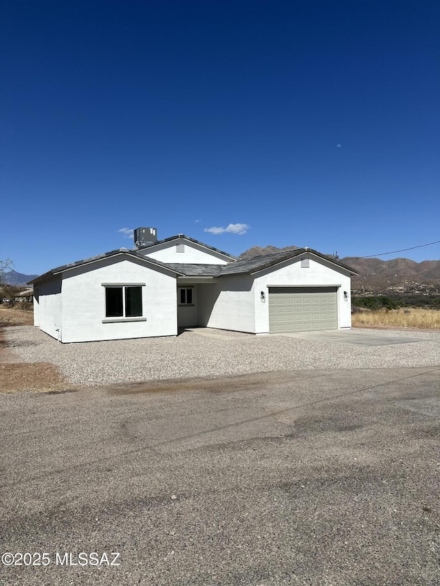 view of front of property featuring driveway, central AC unit, a mountain view, an attached garage, and stucco siding