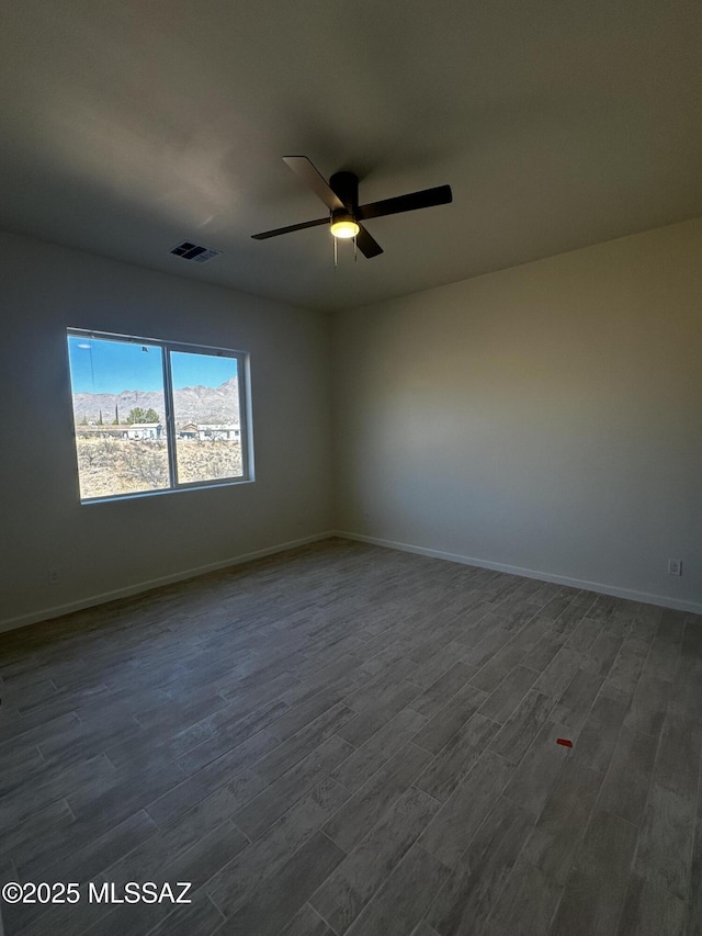 spare room featuring baseboards, ceiling fan, dark wood-style floors, and visible vents
