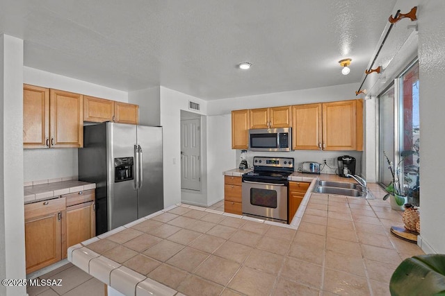 7420 N Oliver Ave, Tucson, AZ 85741 - kitchen featuring tile countertops, visible vents, a sink, a peninsula, and stainless steel appliances