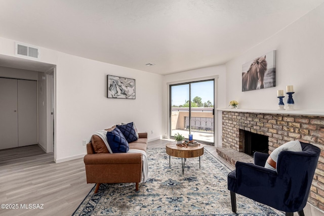 living area featuring baseboards, a fireplace, light wood-type flooring, and visible vents