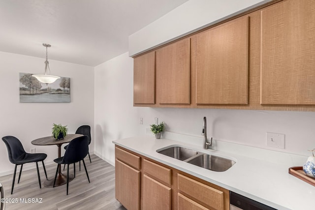 kitchen with decorative light fixtures, a sink, light countertops, baseboards, and light wood-style floors