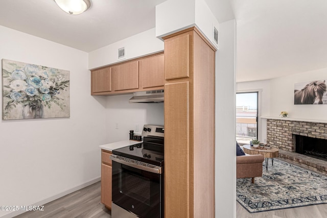 kitchen featuring light wood-style floors, a brick fireplace, electric stove, under cabinet range hood, and visible vents
