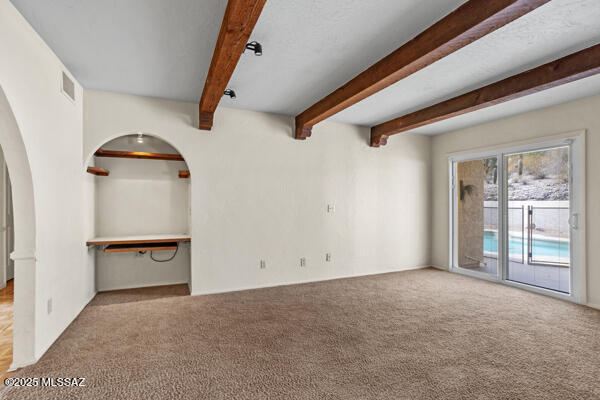 4361 N Wilmot Rd, Tucson, AZ 85750 - unfurnished living room featuring carpet floors, arched walkways, visible vents, and beam ceiling