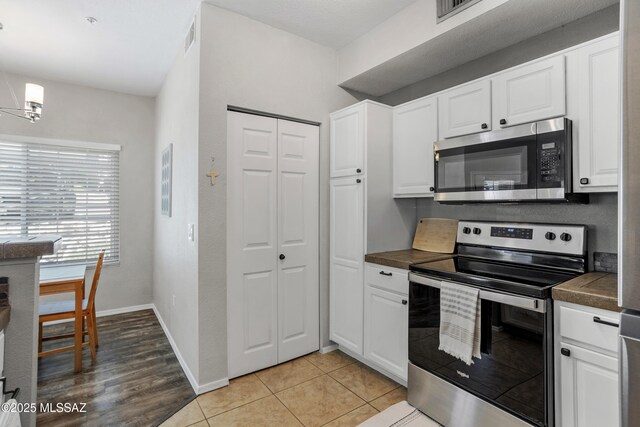 1500 E Pusch Wilderness Dr Unit 10105, Oro Valley, AZ 85737 - kitchen with appliances with stainless steel finishes, dark countertops, white cabinets, baseboards, and a chandelier
