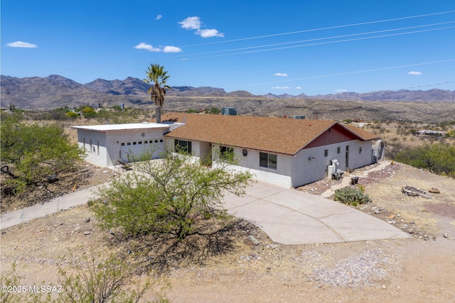 single story home with a mountain view, an attached garage, driveway, and stucco siding