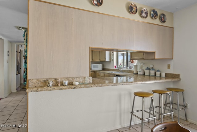 kitchen with a sink, light countertops, a kitchen breakfast bar, light tile patterned floors, and white microwave