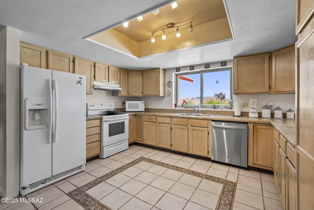 kitchen with white appliances, a textured ceiling, under cabinet range hood, a tray ceiling, and a sink