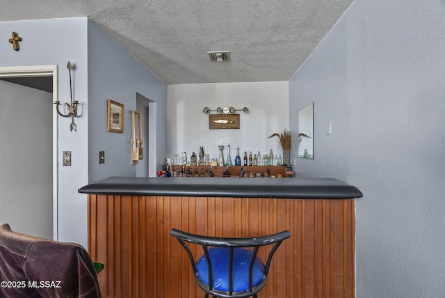bar with a dry bar, a textured ceiling, and visible vents