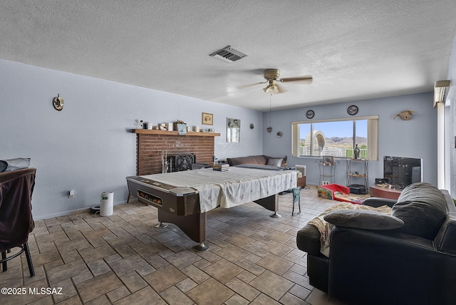 rec room with visible vents, a fireplace, stone finish floor, a textured ceiling, and a ceiling fan