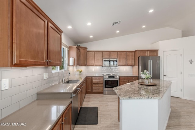 13795 N Buckhorn Cholla Dr, Marana, AZ 85658 - kitchen featuring appliances with stainless steel finishes, a sink, a kitchen island, vaulted ceiling, and brown cabinetry