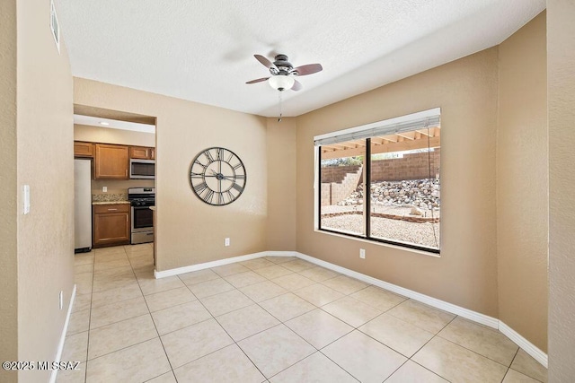 empty room featuring light tile patterned floors, baseboards, a ceiling fan, and a textured ceiling