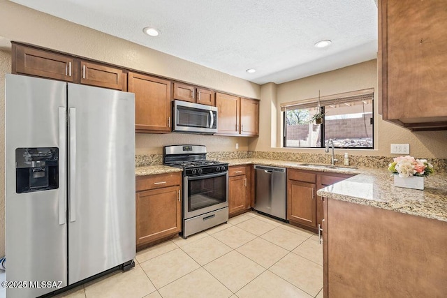 kitchen with appliances with stainless steel finishes, brown cabinetry, light tile patterned floors, and a sink