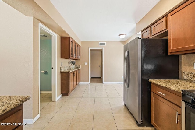 kitchen with freestanding refrigerator, brown cabinetry, and baseboards