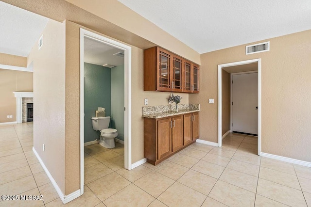interior space with light stone countertops, glass insert cabinets, light tile patterned floors, and visible vents