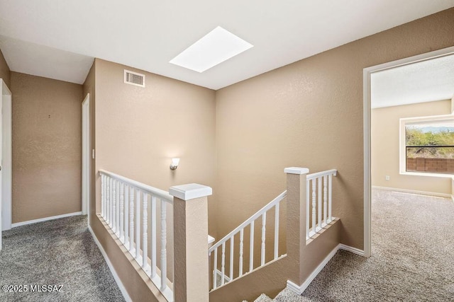 corridor with carpet, visible vents, an upstairs landing, a skylight, and a textured wall