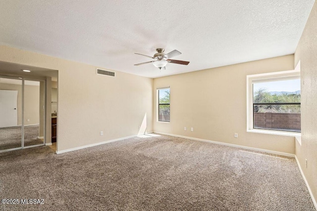 carpeted spare room featuring a textured ceiling, visible vents, baseboards, and ceiling fan