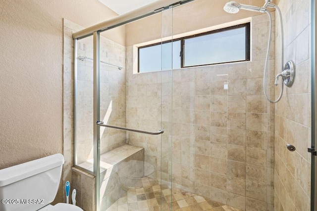full bathroom with toilet, a textured wall, and a shower stall