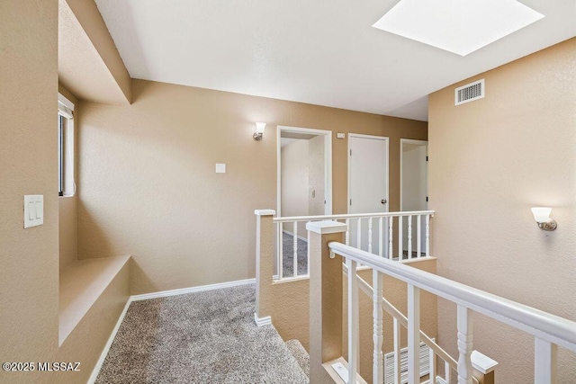 hallway with an upstairs landing, a skylight, carpet floors, visible vents, and baseboards