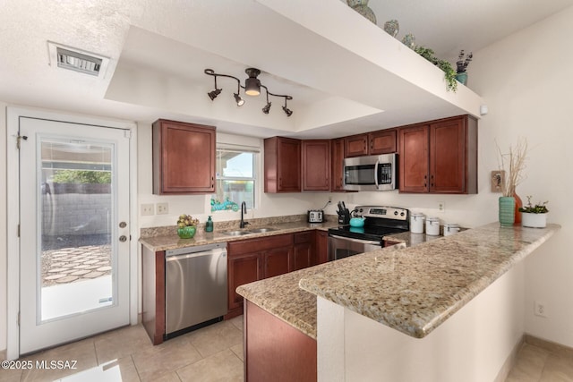 kitchen featuring light stone countertops, a sink, a raised ceiling, a peninsula, and stainless steel appliances