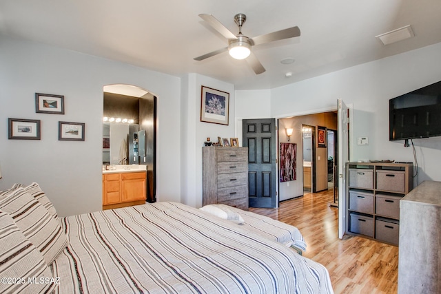 bedroom with ceiling fan, light wood finished floors, ensuite bath, arched walkways, and visible vents