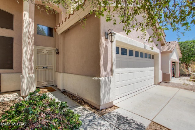 doorway to property with a tiled roof, an attached garage, and stucco siding