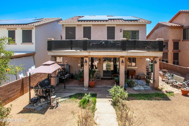 rear view of house featuring stucco siding, roof mounted solar panels, a patio area, and a balcony