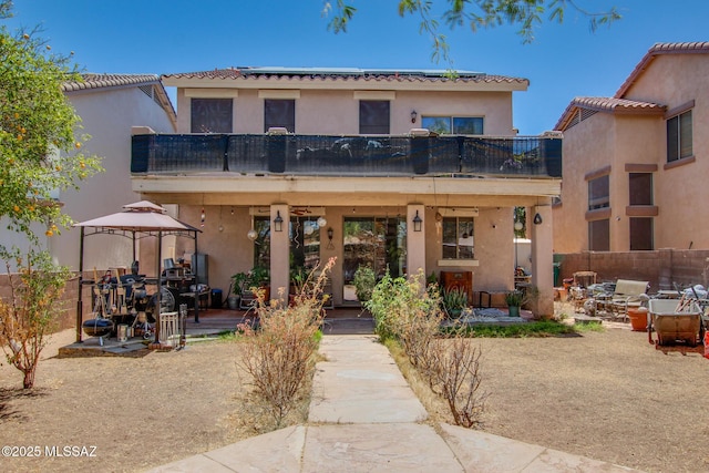 back of house featuring a balcony, a patio, stucco siding, a gazebo, and a tile roof
