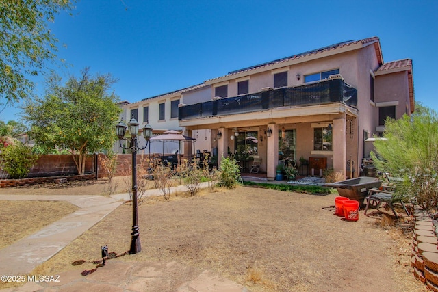rear view of property with fence, a balcony, a patio, stucco siding, and a tile roof