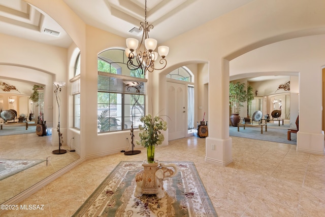 interior space with visible vents, a towering ceiling, arched walkways, a notable chandelier, and a tray ceiling