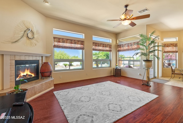 living room with a ceiling fan, visible vents, wood finished floors, and a tile fireplace
