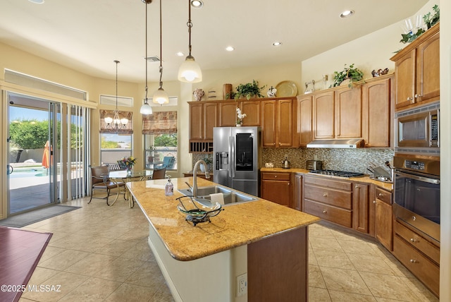 kitchen with a sink, an island with sink, stainless steel appliances, light tile patterned floors, and backsplash