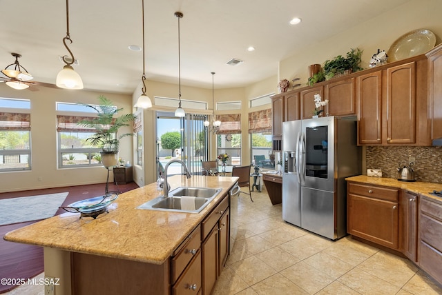 kitchen featuring decorative backsplash, a kitchen island with sink, hanging light fixtures, a sink, and stainless steel appliances