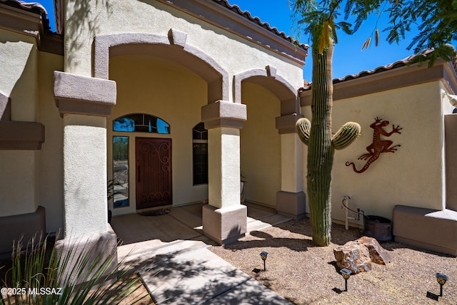 doorway to property featuring covered porch, stucco siding, and a tile roof