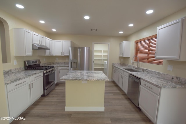 kitchen featuring a kitchen island, appliances with stainless steel finishes, a sink, light stone counters, and under cabinet range hood