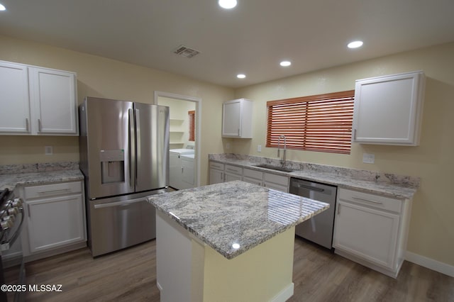 kitchen with independent washer and dryer, visible vents, appliances with stainless steel finishes, wood finished floors, and a sink