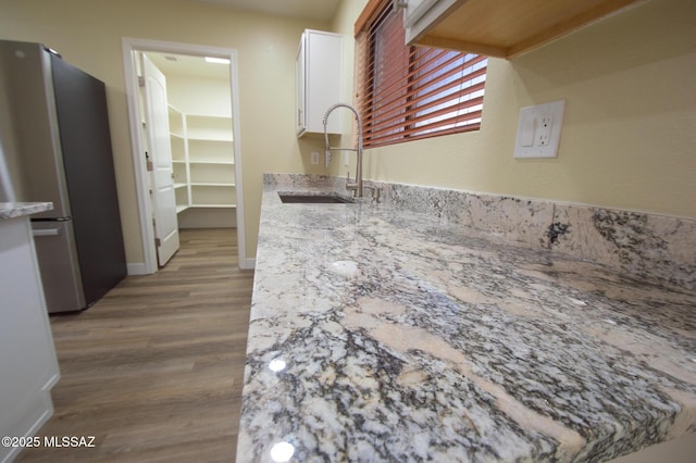 kitchen featuring a sink, freestanding refrigerator, white cabinetry, baseboards, and wood finished floors