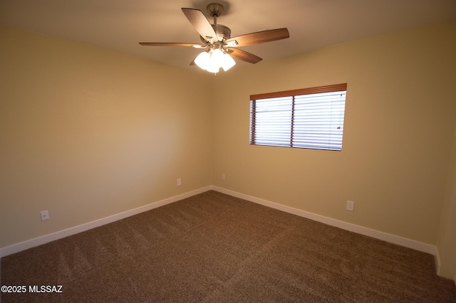 empty room with dark colored carpet, a ceiling fan, and baseboards