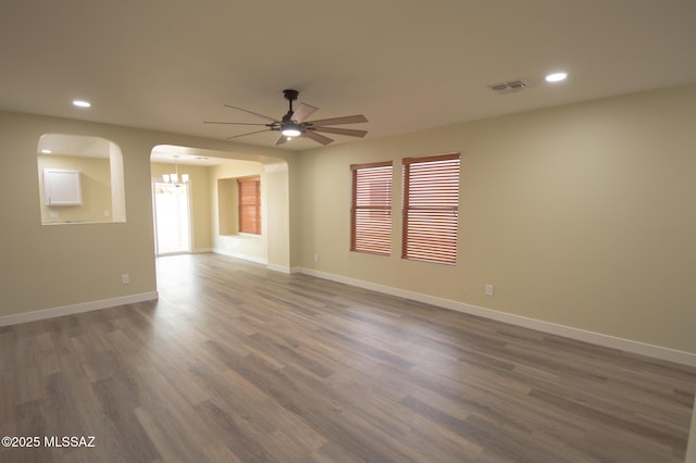 empty room with visible vents, dark wood-style flooring, baseboards, recessed lighting, and ceiling fan with notable chandelier