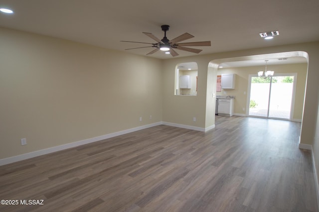 unfurnished living room featuring wood finished floors, baseboards, recessed lighting, arched walkways, and ceiling fan with notable chandelier