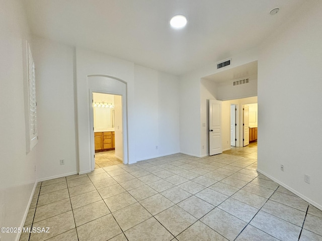unfurnished room featuring visible vents, arched walkways, and light tile patterned flooring